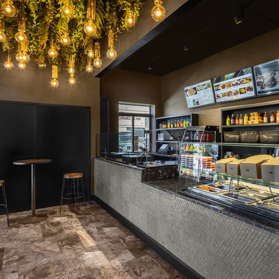 Interior of Bamboo Walk Caribbean Restaurant with a counter, menu screens, and decorative hanging lights.