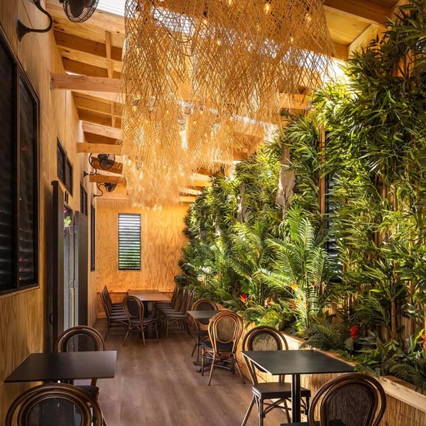 Bamboo Walk Caribbean Restaurant interior with wooden walls, lush green plants, and rattan light fixtures.