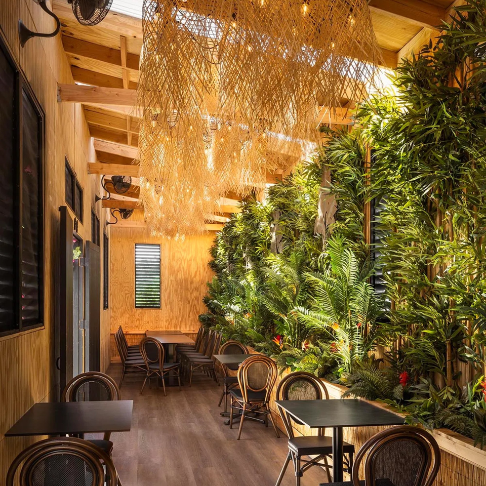 Bamboo Walk Caribbean Restaurant interior with wooden walls, lush green plants, and rattan light fixtures.