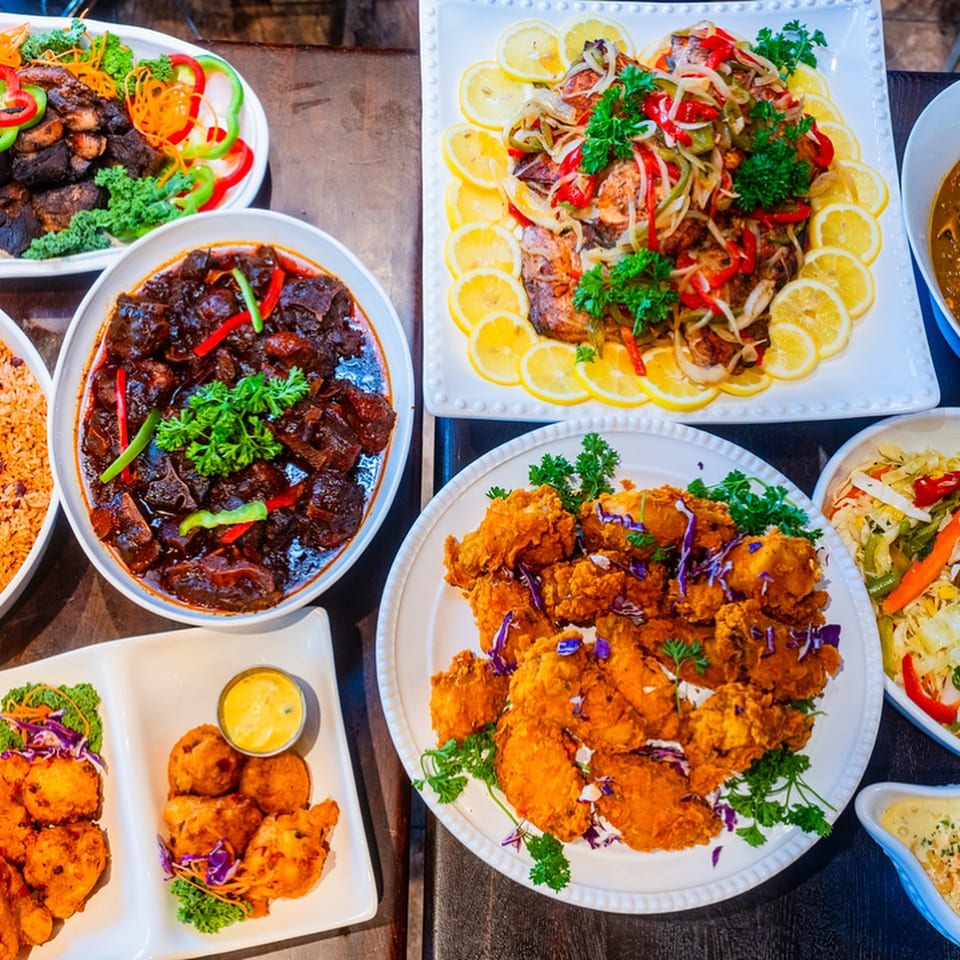 A vibrant spread of Caribbean dishes, including fried fish, stew, and fried chicken, on a dark wooden table.