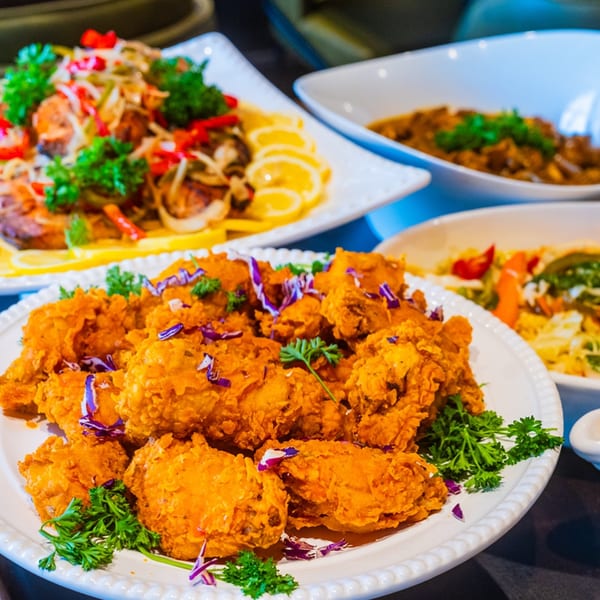 A platter of crispy fried chicken with parsley and purple cabbage, alongside other Caribbean dishes.