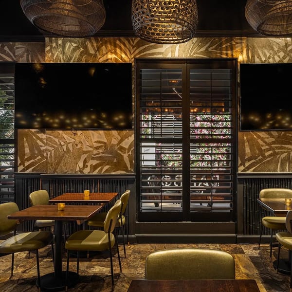 Bamboo Walk Caribbean Restaurant interior with dark wood tables, green chairs, and tropical leaf wallpaper.