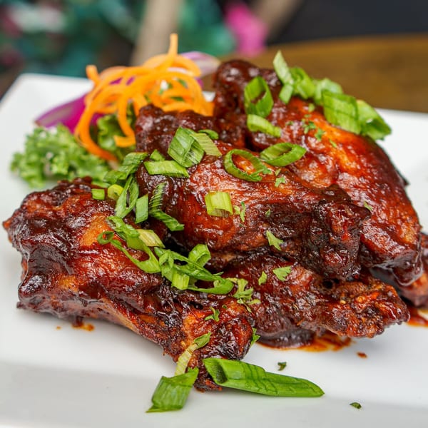 Caribbean BBQ chicken wings, glazed with sauce and topped with fresh green onions, served on a white plate.