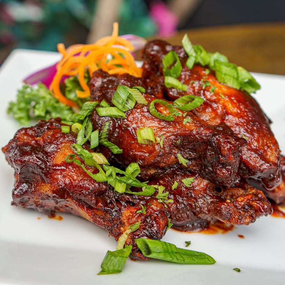 Caribbean BBQ chicken wings, glazed with sauce and topped with fresh green onions, served on a white plate.